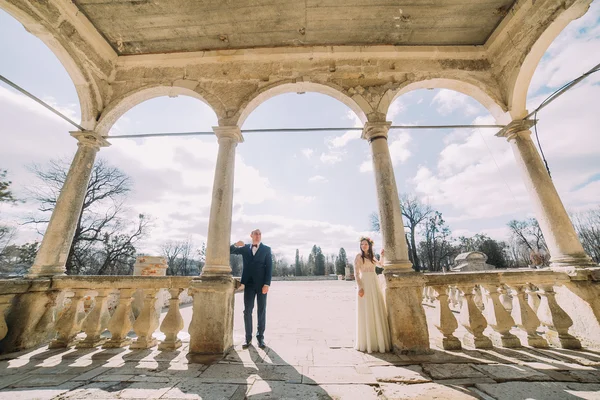 アンティークの荒廃した宮殿のアーチ型テラスでポーズをとる結婚式のカップル — ストック写真