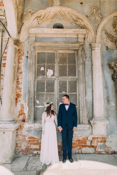 Жених и невеста улыбаются, стоя в старом разрушенном кирпичном окне древнего здания — стоковое фото