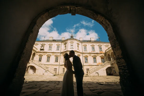 Passionate enloved couple share romantic at entrance arch of magnificent looking baroque palace shined by bright summer sun rays — Stock Photo, Image