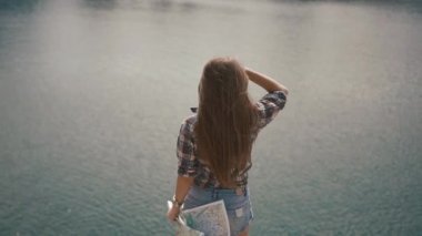 Güzel genç aktif backpacker kız güneşli bir günde dağ gölünün su yüzeyine yakın harita ile kontrol