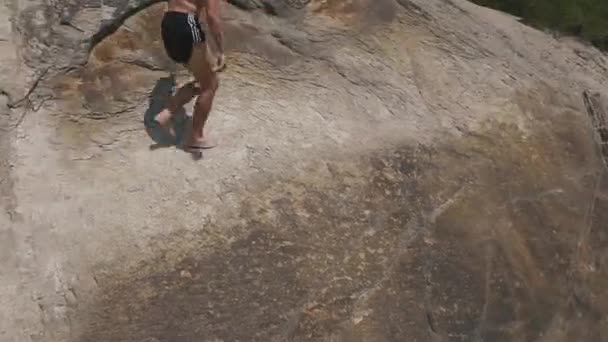Giovane uomo saltando sulle rocce vicino riva del lago e saltando dalla scogliera in acqua. Stile di vita divertente estate — Video Stock