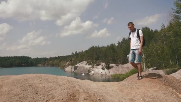 Молодой турист ходит по скалистым холмам около озера в горах, проверяя свой путь с бумажной картой — стоковое видео