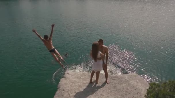 Enloved ティーンエイ ジャーのカップルが水の表面の近くの大きな岩にジャンプや入浴若者たちとキスします。スローモーション — ストック動画