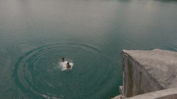 Хлопчик-підліток стрибає зі скелі до свого друга у воду. Літній веселий спосіб життя — стокове відео