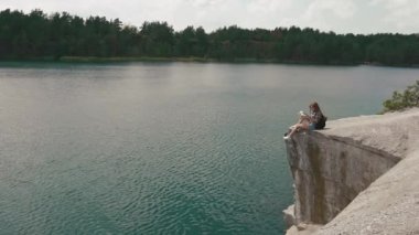 Genç aktif backpacker kız dağ kayanın üzerine dağ Orman Gölü büyük su yüzeyi üzerinde bekleterek rahatlatır