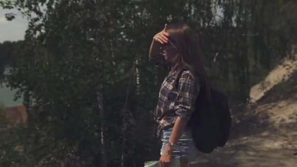 Jeune femme touristique attrayante avec sac à dos regardant sa carte et levant les yeux vérifier avec le terrain local. Caméra tourne autour — Video