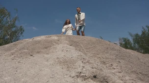 Belle paire aimée posant en plein air au bord du lac en vêtements traditionnels ukrainiens. Jeune couple courant sur une colline rocheuse — Video