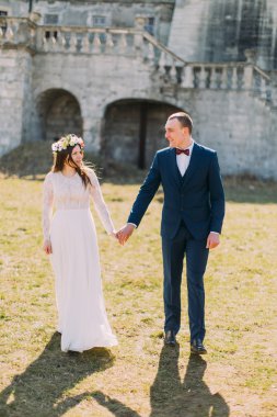 Büyüleyici yeni evli gelin ve damat güzel harap barok saray yakınında yeşil güneşli çim üzerinde elleri ile birbirlerine tutarak