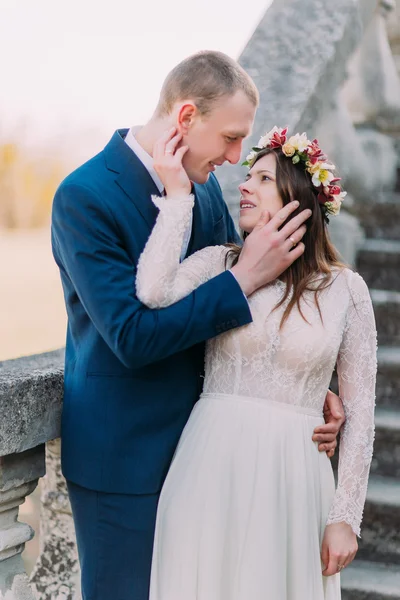 Feliz novio abrazándose con su novia bonita mientras ambos se paran en escaleras de piedra antiguas. Retrato de media longitud — Foto de Stock