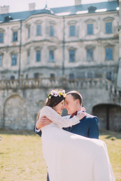 Jolie paire de jeunes mariés à la pelouse verte près du magnifique palais baroque en ruine. Marié aimant tenant charmante mariée sur ses mains — Photo