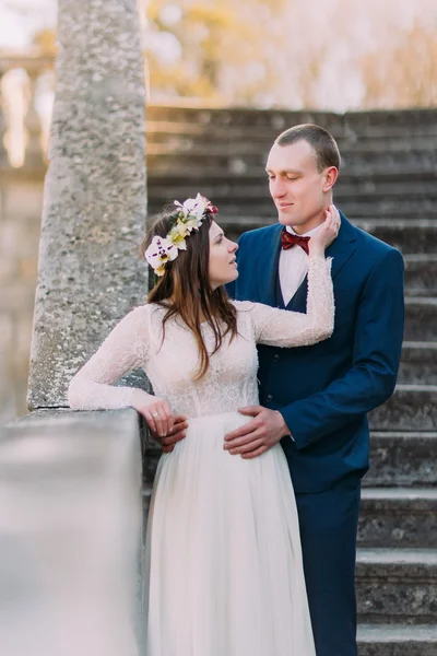 Feliz novio sosteniendo a su novia bonita mientras ambos se paran en escaleras de piedra antiguas. Retrato de medio cuerpo — Foto de Stock