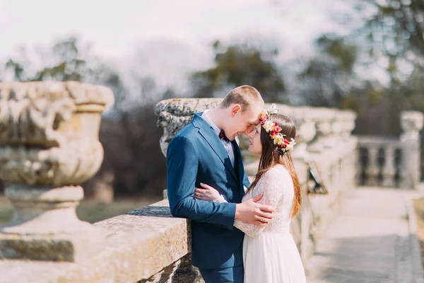 Свадебный портрет молодоженов, позирующих на старой каменной террасе в весеннем парке и любовно трогающих лбы — стоковое фото
