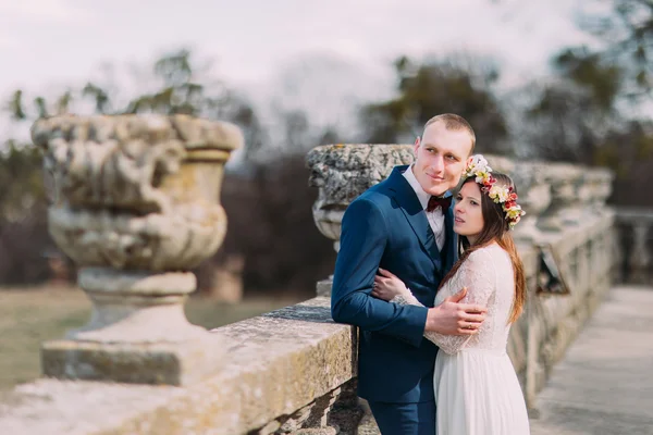 Retrato de boda de pareja recién casada con estilo posando en la antigua terraza de piedra en el parque de primavera y sosteniéndose mutuamente — Foto de Stock