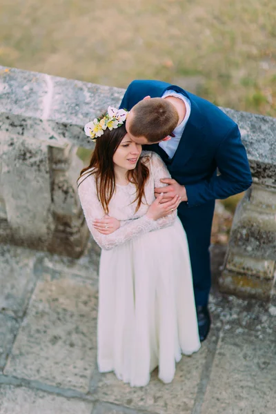 Счастливый жених целует свою милую маленькую невесту, в то время как оба стоят на старинной каменной лестнице. Вид сверху — стоковое фото
