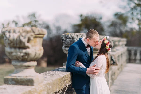 Portrait de mariage d'un couple de jeunes mariés élégants s'embrassant passionnément sur une vieille terrasse en pierre dans un parc de printemps — Photo