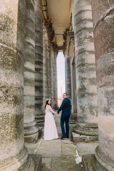 Joven pareja atractiva boda posando entre filas de columnas de piedra de construcción antigua —  Fotos de Stock