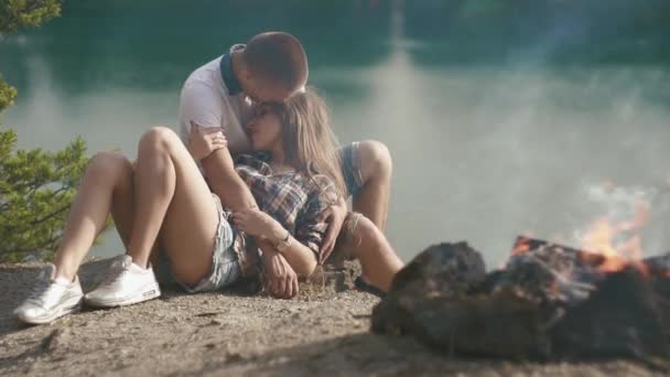 Любящие подростки обнимаются во время отдыха в кемпинге на лесном берегу. Костер на переднем плане — стоковое видео