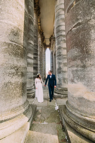 Junges Hochzeitspaar posiert zwischen Reihen antiker Bausäulen — Stockfoto