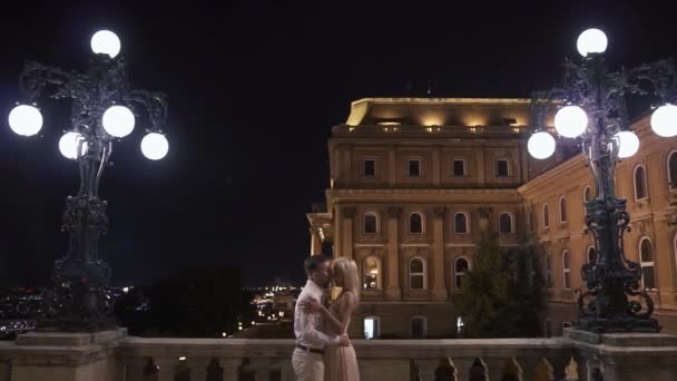 Fantastisch paar in liefde omarmen op het balkon op de nacht oude stad achtergrond — Stockvideo