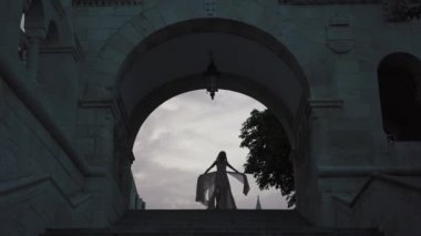 Muhteşem gelin silueti zarif alacakaranlıkta kalede antik kemer altında dans.