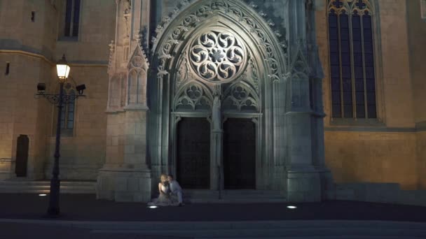 Romantic, sensual newlywed couple sitting at the doorway of ancient gothic church — Stock Video