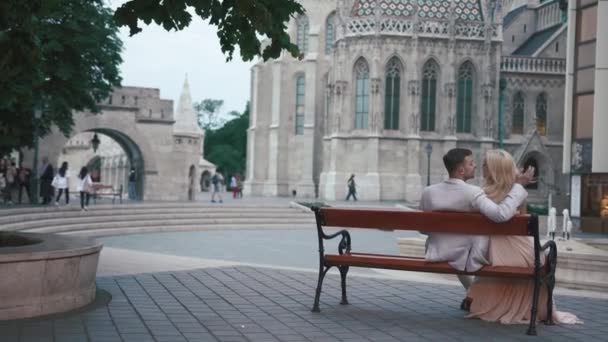 Joyeux jeune couple amoureux assis sur le banc et embrassant sur le fond de magnifique château blanc antique — Video