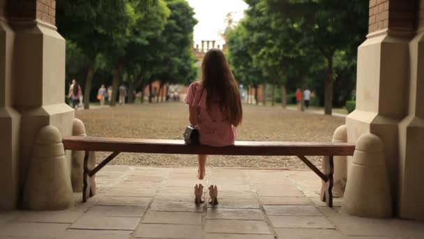 Teenager-Mädchen, das sich in der Natur auf eine Bank setzt und barfuß mit überkreuzten Beinen ein Buch liest. zurück