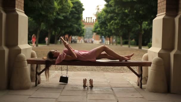 Ragazza adolescente sdraiato sulla panchina nel campus universitario e la lettura di un libro a piedi nudi — Video Stock