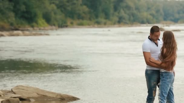 Mooie jonge paar omarmen in de buurt van grote rivier op stenen bank — Stockvideo