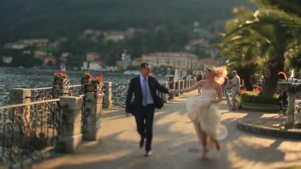 Жених и невеста бегут вдоль набережной — стоковое видео