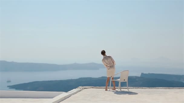 Schöne sexy brünette Braut in Robe sitzt auf dem Dach mit Meer und Bergen im Hintergrund — Stockvideo