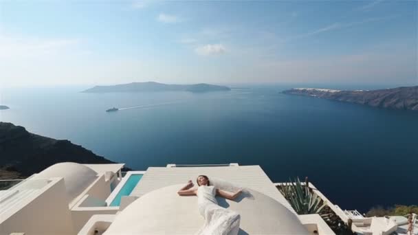 Beautiful brunette bride lying on the terrace in white dress with sea background — Stock Video