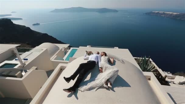 Morena novia y novio tumbado en la terraza en vestido blanco con fondo de mar — Vídeos de Stock