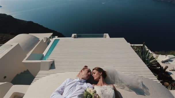 Brünette Braut und Bräutigam auf der Terrasse liegend in weißem Kleid mit Meereshintergrund — Stockvideo