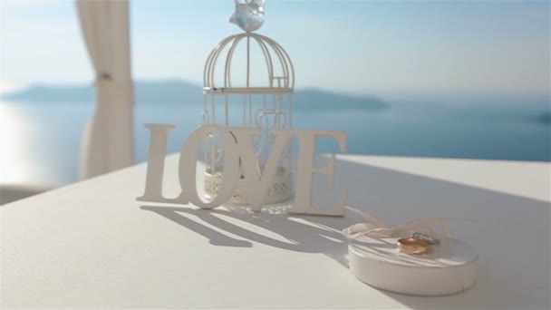 Vacker bröllop tält mittgång på kusten med vigselringar på bordet och havet med bergen bakgrund — Stockvideo