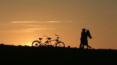 Romantik Çift Tandem günbatımı öpüşme bisiklet ile. Yaz doğa arka plan güzel bulutlar gökyüzünde ile yakın çekim