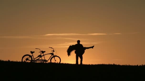 Silhouette de beau couple avec vélos tandem. Homme dansant la tenant dans ses bras pendant le coucher du soleil. Été Nature Fond avec de beaux nuages dans le ciel Gros plan — Video