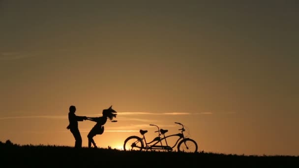 Silhouette de beau couple avec des vélos tandem dansant tenant la main contre le coucher de soleil fabuleux Fond d'écran Gros plan — Video