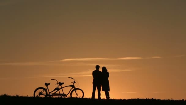 Silueta de pareja romántica con bicicletas en tándem mirando y disfrutando de la puesta de sol apoyados juntos — Vídeos de Stock