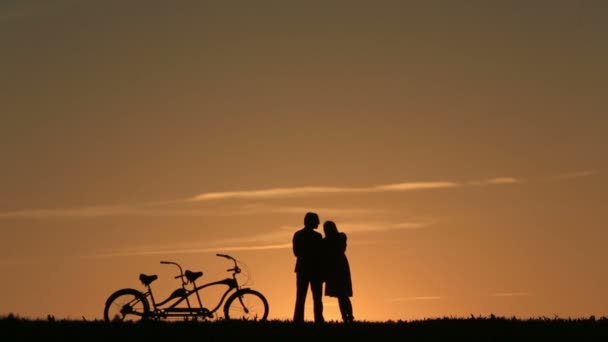 Silueta de pareja romántica con bicicletas en tándem mirando y disfrutando de la puesta de sol apoyados juntos — Vídeos de Stock