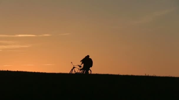 Silueta de hermosa pareja con bicicletas en tándem jugando a la captura contra el atardecer en el fondo — Vídeos de Stock