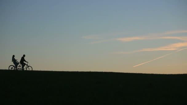 Silhouette eines schönen Paares, das bei Sonnenuntergang mit dem Tandemfahrrad unterwegs ist. Sommer Natur Hintergrund mit schönen Wolken am Himmel aus nächster Nähe — Stockvideo