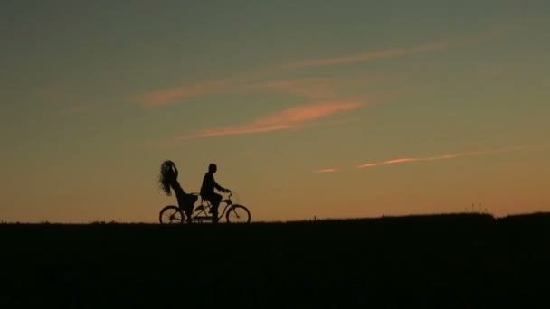 タンデムに乗って美しいカップルのシルエットが夕日自転車します。空に雲が美しい、夏の自然の背景をクローズ アップ. — ストック動画