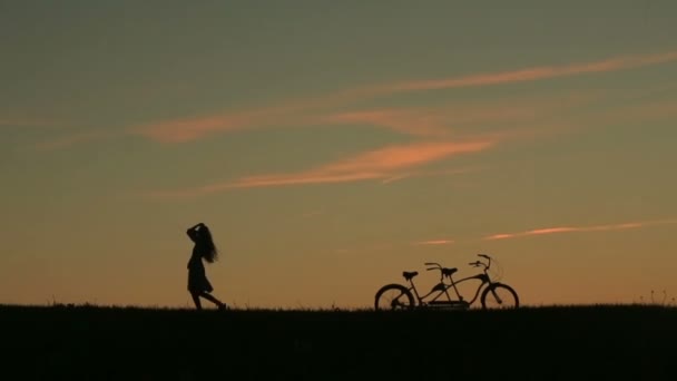 Silueta de hermosa pareja con bicicleta en tándem. Chica graciosamente se aleja mientras su novio la sigue y la besa — Vídeos de Stock