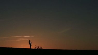 İki kişilik bisiklet ile güzel çift silüeti. Adam onu kollarında tutar süre günbatımı. Yaz doğa arka plan güzel bulutlar gökyüzünde ile yakın çekim