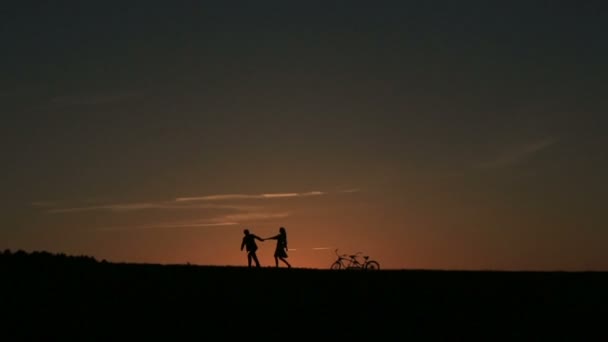 Silueta nádherný pár s tandemové kolo chůze a držení rukou při západu slunce. Letní přírodní pozadí krásné mraky na obloze zblízka — Stock video