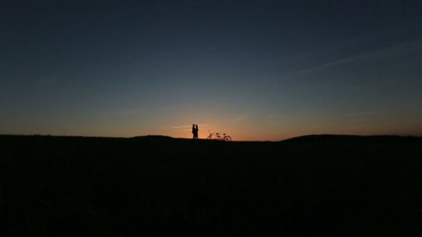 Pareja romántica con tándem bicicleta besos mientras puesta del sol. Fondo de la naturaleza de verano con hermosas nubes en el cielo de cerca — Vídeos de Stock