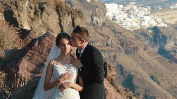 結婚されていたカップル、花嫁と花婿、サントリーニ島、ギリシャの山火山景観にキスをクローズ アップ. — ストック動画