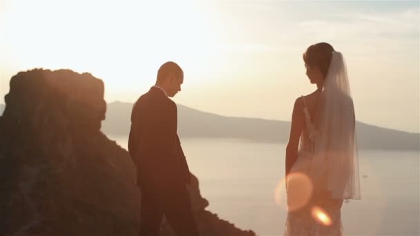 Stilig brudgummen och hans charmiga bruden tittar på utsikten på toppen av kullen på sunset himmel bakgrund — Stockvideo