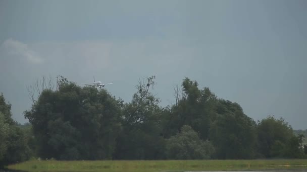 Letadlo přistane v modré zatažené obloze se stromy kymácející na pozadí — Stock video